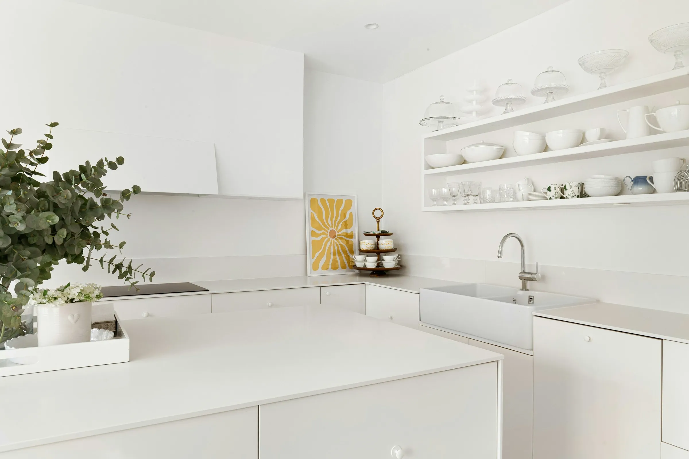 Minimalist all-white kitchen with seamless white worktops, a kitchen island, and open shelving