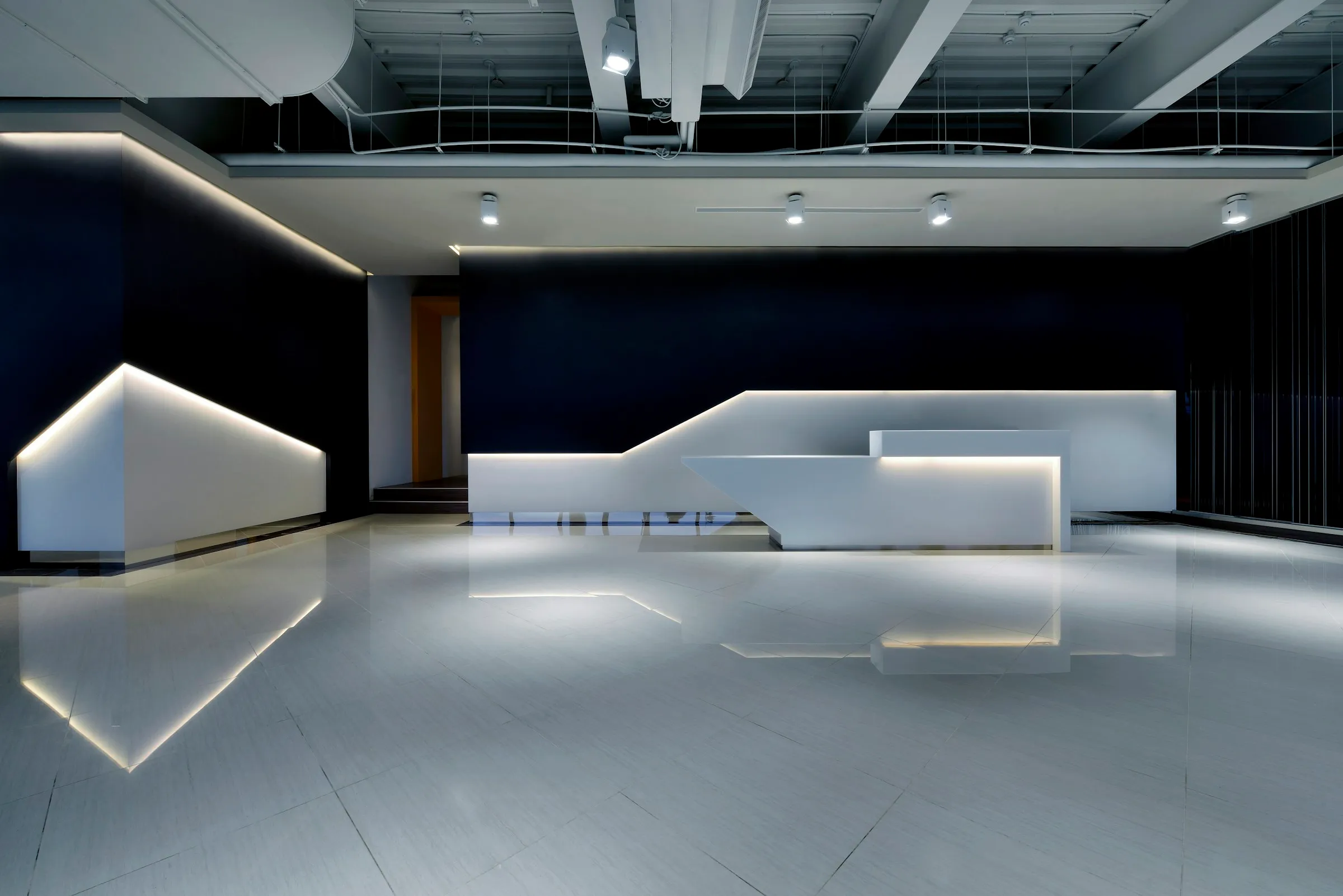 Angular white solid-surface reception counter with LED strip lighting in a dark lobby (reference photo)